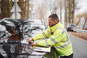 Male police officer in green uniform putting fine list to the vehicle photo