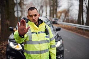 oficial de policía masculino con uniforme verde que muestra un gesto de parada cerca del vehículo foto