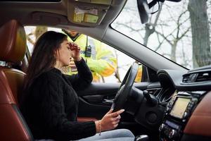 chicas se siente mal. oficial de policía masculino con uniforme verde revisando el vehículo en la carretera foto