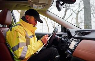 Male police officer in green uniform sitting in automobile and working with documents photo