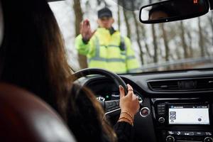 un oficial de policía con uniforme verde detiene un vehículo con una conductora en la carretera foto