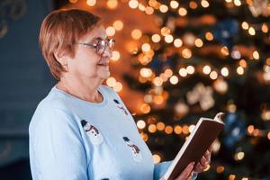 retrato de abuela que de pie en la habitación decorada de año nuevo con libro foto