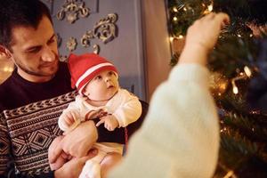 Father and mother with their child decorating tree together in room photo