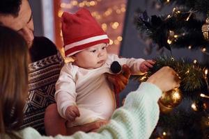 Father and mother with their child decorating tree together in room photo