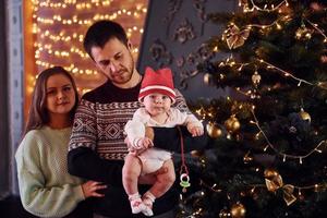 Father and mother with their child decorating tree together in room photo