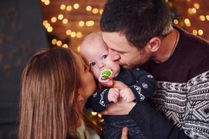 Father and mother kissing their child in christmas decorated room photo