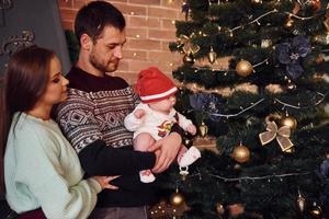 padre y madre con su hijo juntos en una habitación decorada con navidad foto