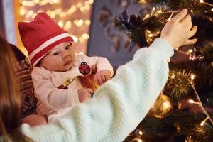 Father and mother with their child decorating tree together in room photo