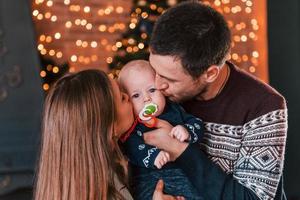 Father and mother kissing their child in christmas decorated room photo