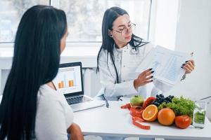 Female nutritionist with laptop gives consultation to patient indoors in the office photo