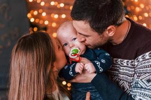 Father and mother kissing their child in christmas decorated room photo