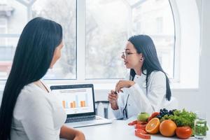 Female nutritionist with laptop gives consultation to patient indoors in the office photo