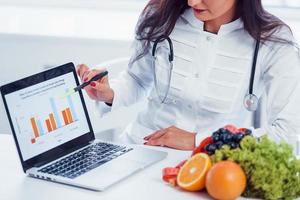 Female nutritionist in white coat sitting indoors in the office at workplace with laptop photo