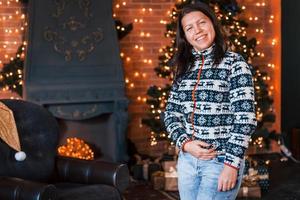 Happy woman in christmas clothes standing in the New year decorated room photo