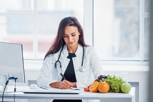 Female nutritionist in white coat sitting indoors in the office at workplace photo