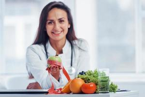 nutricionista femenina con bata blanca sentada en el interior de la oficina en el lugar de trabajo foto