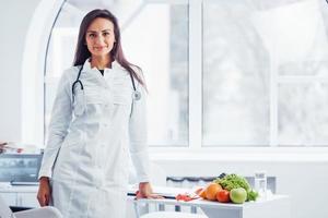 Female nutritionist in white coat sitting indoors in the office at workplace photo