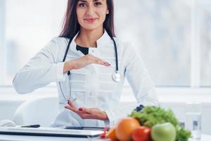 Female nutritionist in white coat sitting indoors in the office at workplace photo