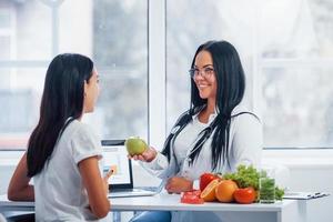 Female nutritionist with laptop gives consultation to patient indoors in the office photo