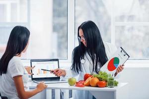 Female nutritionist with graph gives consultation to patient indoors in the office photo