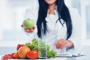 Female nutritionist in white coat holding apple in hand photo