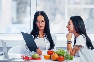 Female nutritionist gives consultation to patient indoors in the office by using notepad photo