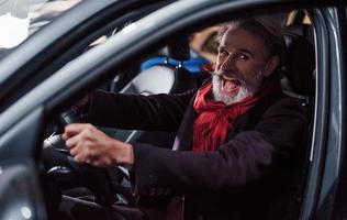 Happy stylish senior man with grey hair and mustache is in the modern car photo