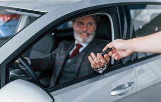 un anciano moderno y elegante con pelo gris y bigote está en el coche moderno foto