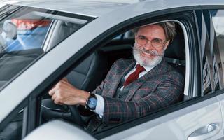 feliz anciano elegante con pelo gris y bigote está en el coche moderno foto