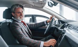 un anciano moderno y elegante con pelo gris y bigote está en el coche moderno foto