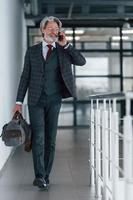 hombre de negocios de alto nivel con traje y corbata con cabello gris y barba caminando adentro con una bolsa foto