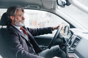 un anciano moderno y elegante con pelo gris y bigote está en el coche moderno foto