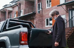 Fashionable senior man with gray hair and beard closes trunk of his car photo