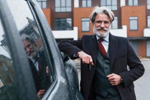 Fashionable senior man with gray hair and beard leaning on his car and holding keys photo