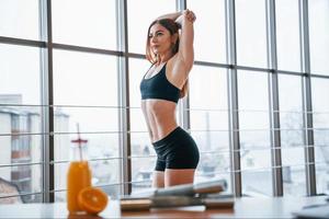 Woman with sportive body standing indoors near table with orange juice and dumbbells photo