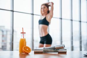 Woman with sportive body standing indoors near table with orange juice and dumbbells photo
