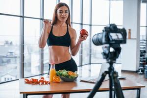 Female vlogger with sportive body standing indoors near table with healthy food photo