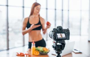 Female vlogger with sportive body standing indoors near table with healthy food photo