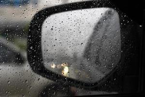 gota de lluvia en el cristal del coche. borroso del ala del espejo con la luz de los faros del coche brilló dos veces. foto