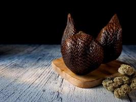 Salak es un tipo de fruta de palma que se come comúnmente. fruto de serpiente, su nombre científico es salacca zalacca. fondo de madera blanca. foto