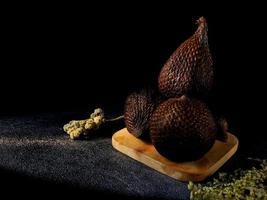 Salak es un tipo de fruta de palma que se come comúnmente. fruto de serpiente, su nombre científico es salacca zalacca. fondo de arena negra. foto
