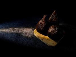 Salak es un tipo de fruta de palma que se come comúnmente. fruto de serpiente, su nombre científico es salacca zalacca. fondo de arena negra. foto