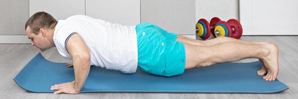 A strong, healthy man with muscles, training at home in the plank position. Fitness at home. Banner photo
