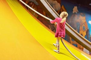 The toddler girl climbs the rope on the slide. Playground, happy childhood photo