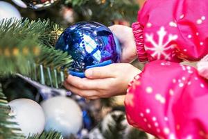 las manos de los niños sostienen en sus palmas una bola azul en un árbol de navidad.vacaciones navideñas foto