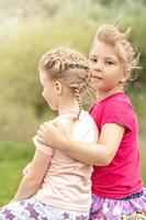 Two girls toddler sisters sit hugging on the bridge in the park. Support photo