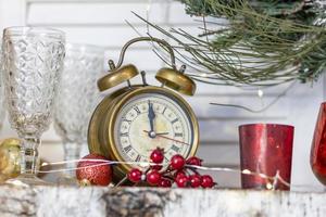 There is an alarm clock with Christmas decorations on the shelf. On the clock five minutes before the new year, Christmas photo