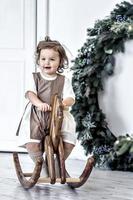 A little girl swings on a wooden horse in the room against the background of Christmas decorations. photo