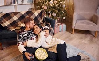 Una pareja joven en el interior de una habitación decorada con Navidad se divierten juntos y celebran el año nuevo foto