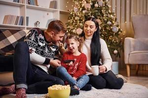 familia feliz adentro en una habitación decorada con navidad celebrando el año nuevo con palomitas de maíz foto